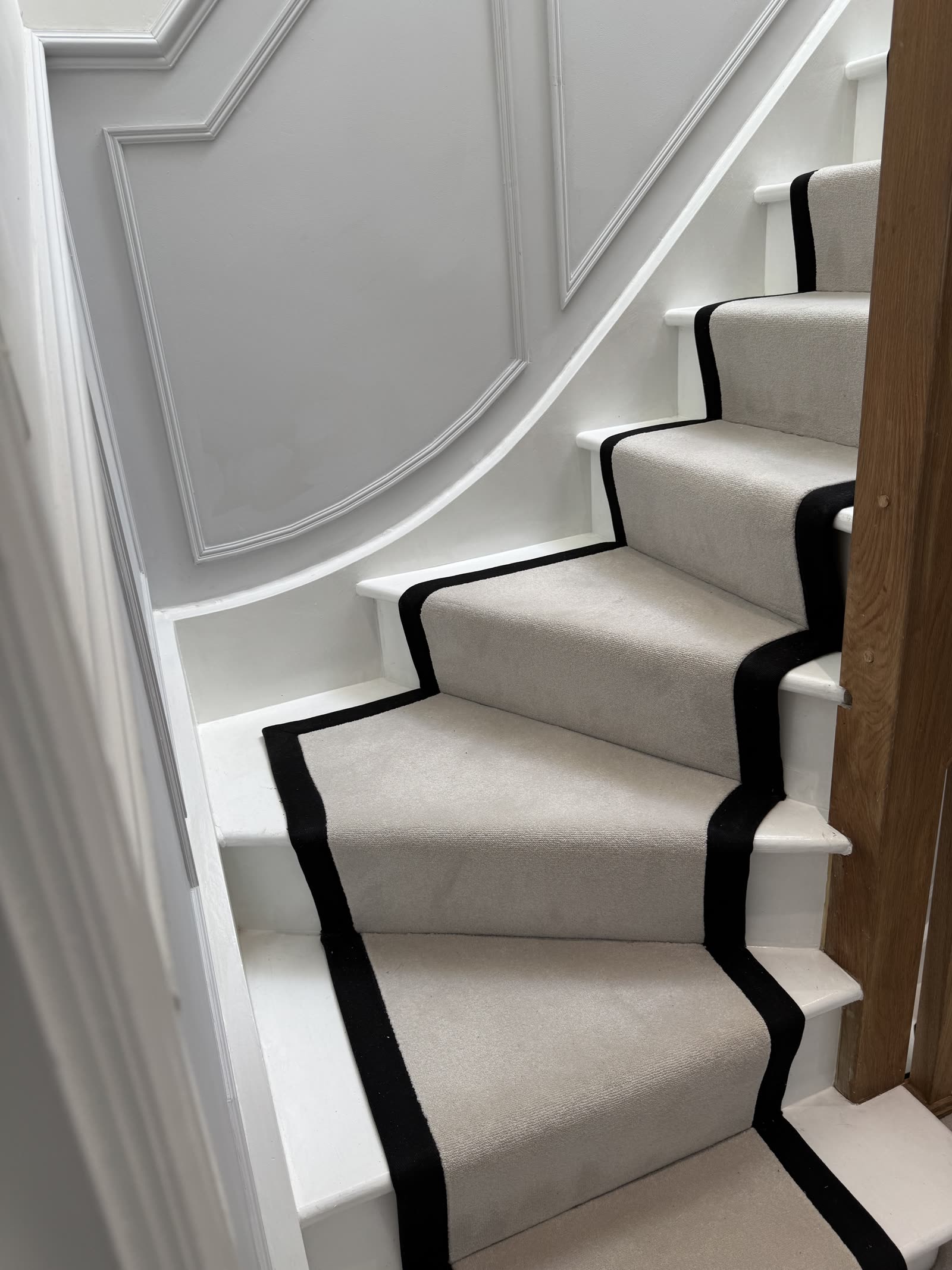 Overhead view of cream-and-black stair runner on white panelled stairwell.