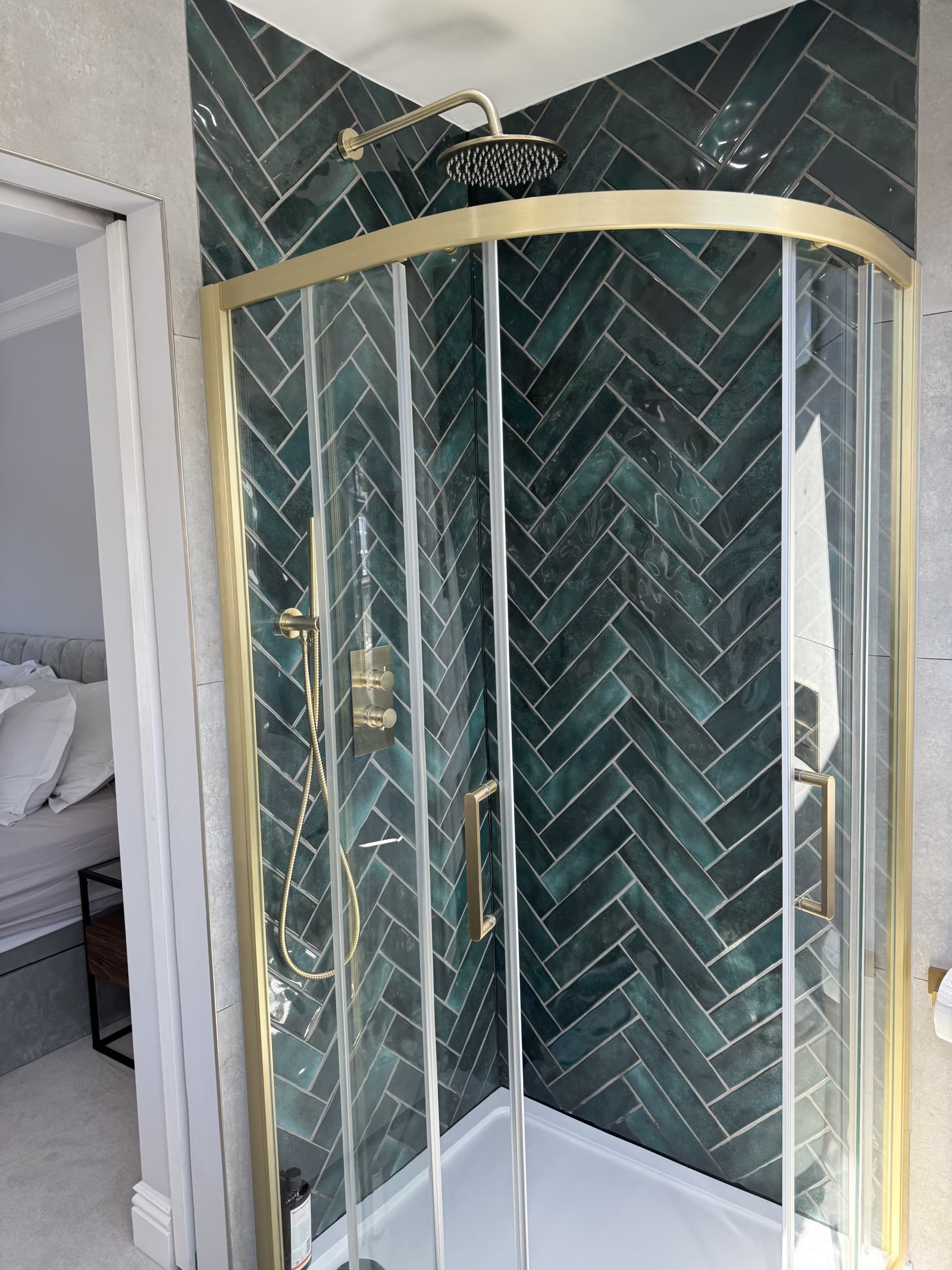 Walk-in shower with green herringbone tile and brass-trimmed glass enclosure.