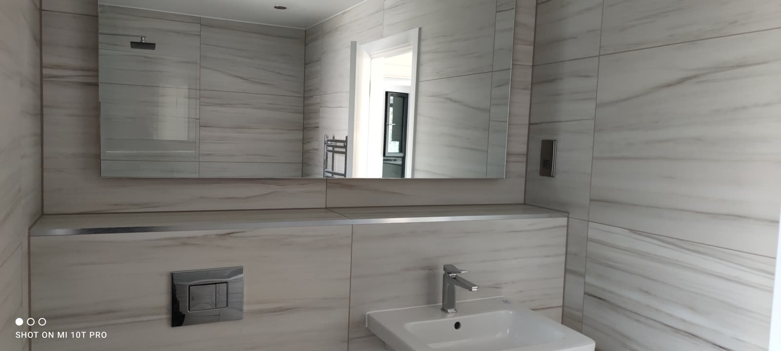 Marble-tiled ensuite with frameless mirror, wall-mounted basin and chrome fittings.