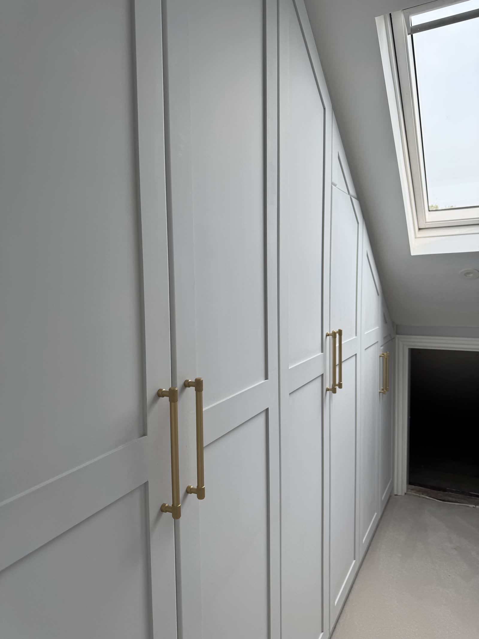 Bespoke built-in wardrobes with brass bar handles, recessed-panel doors and skylight.