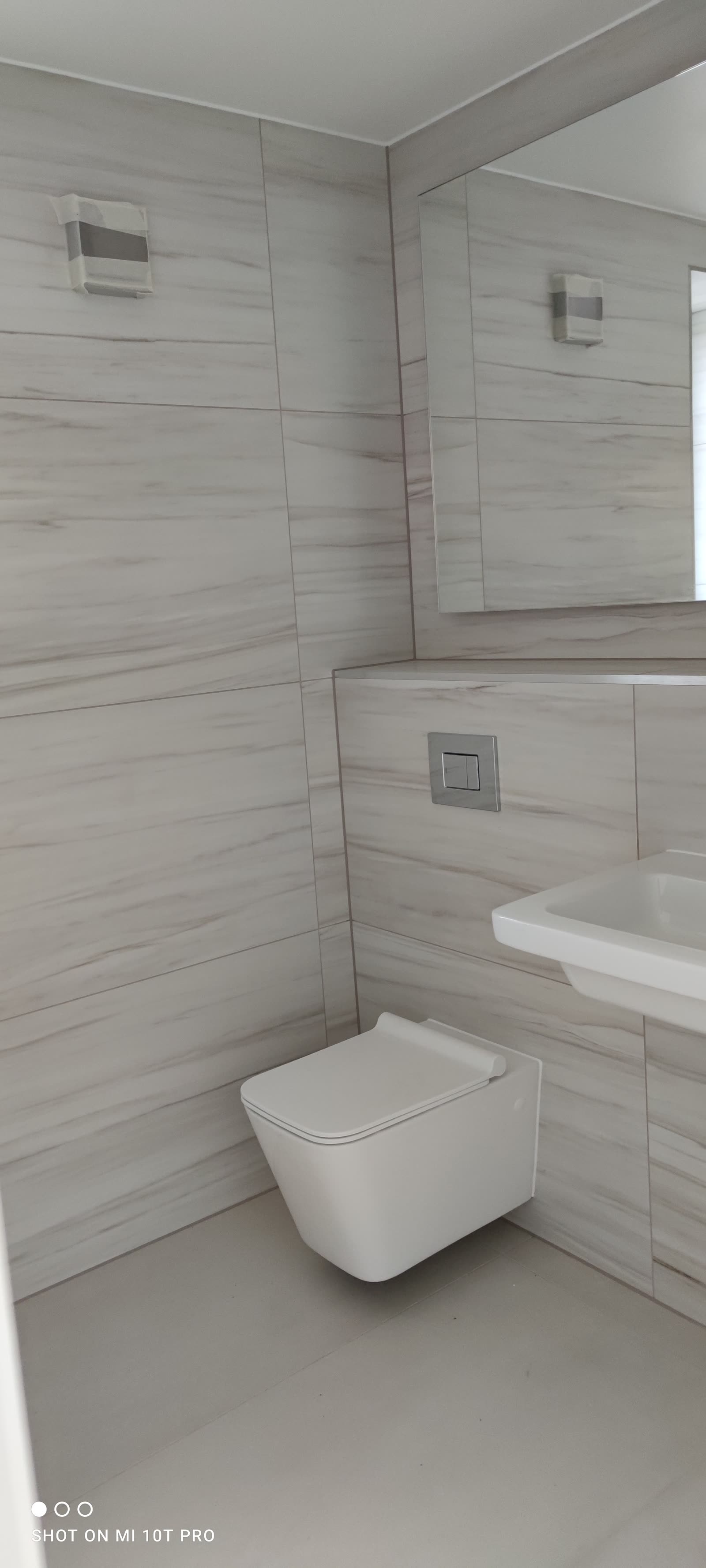 Marble-tiled cloakroom with wall-hung WC and frameless mirror.