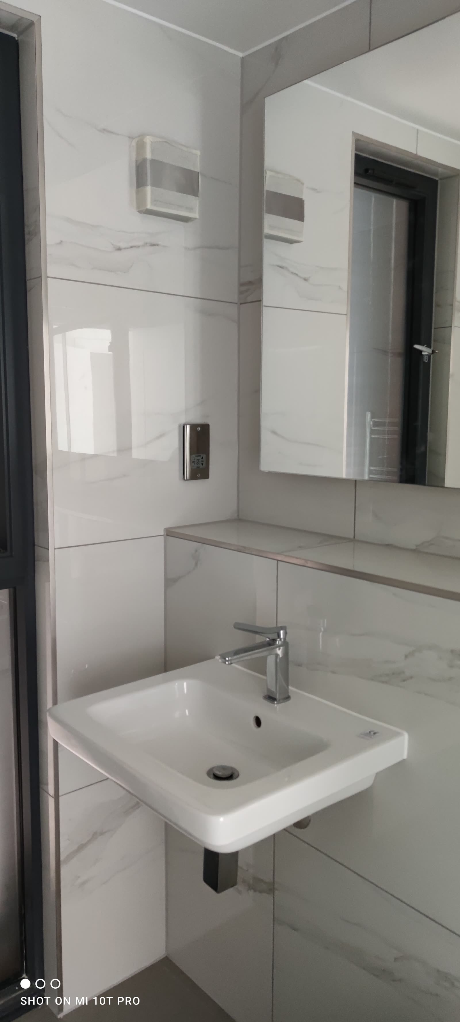 Marble-tiled bathroom with wall-mounted ceramic basin and tall frameless mirror.