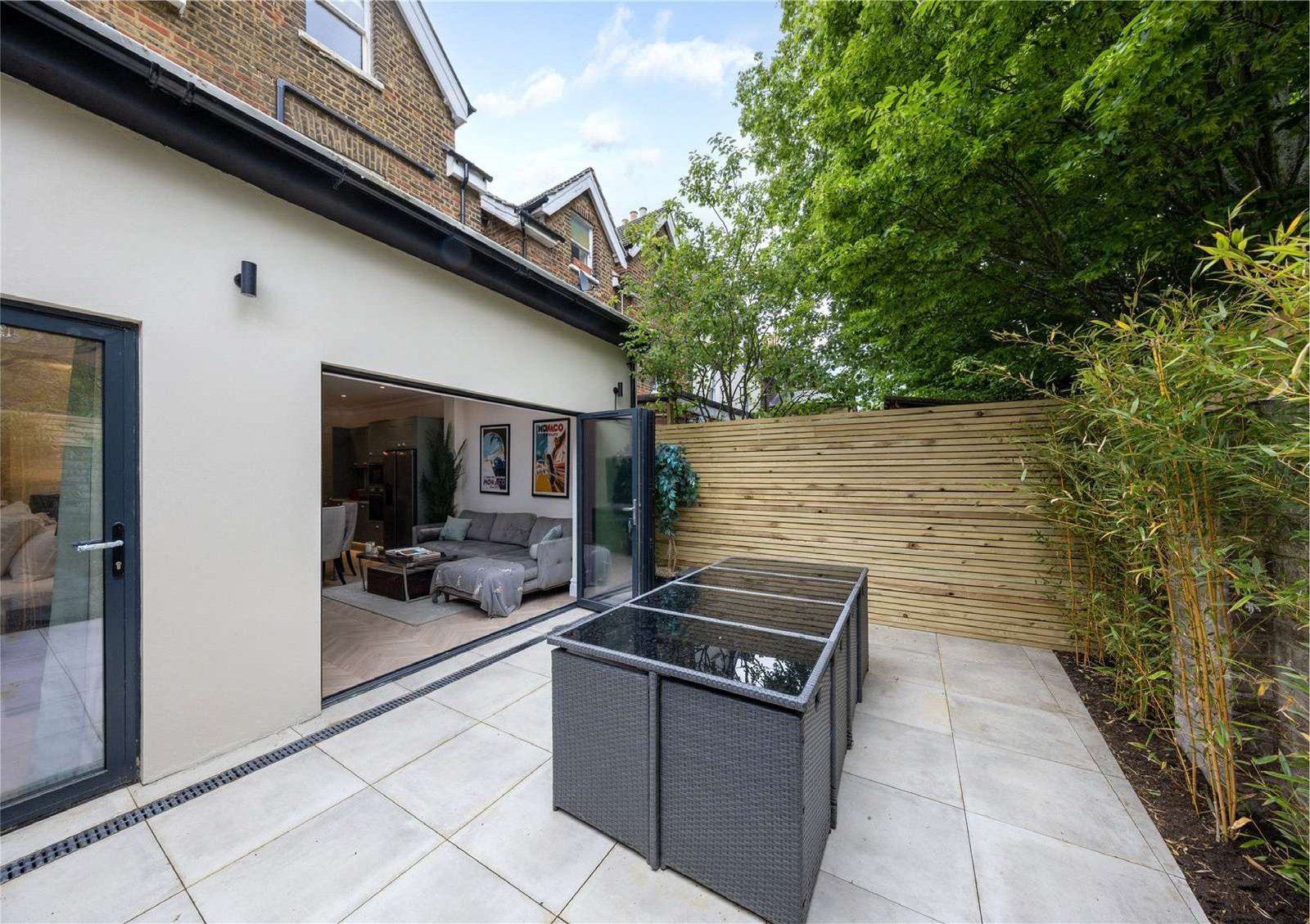 Private patio garden with light paving, rattan furniture and bamboo screening — Flat 1.