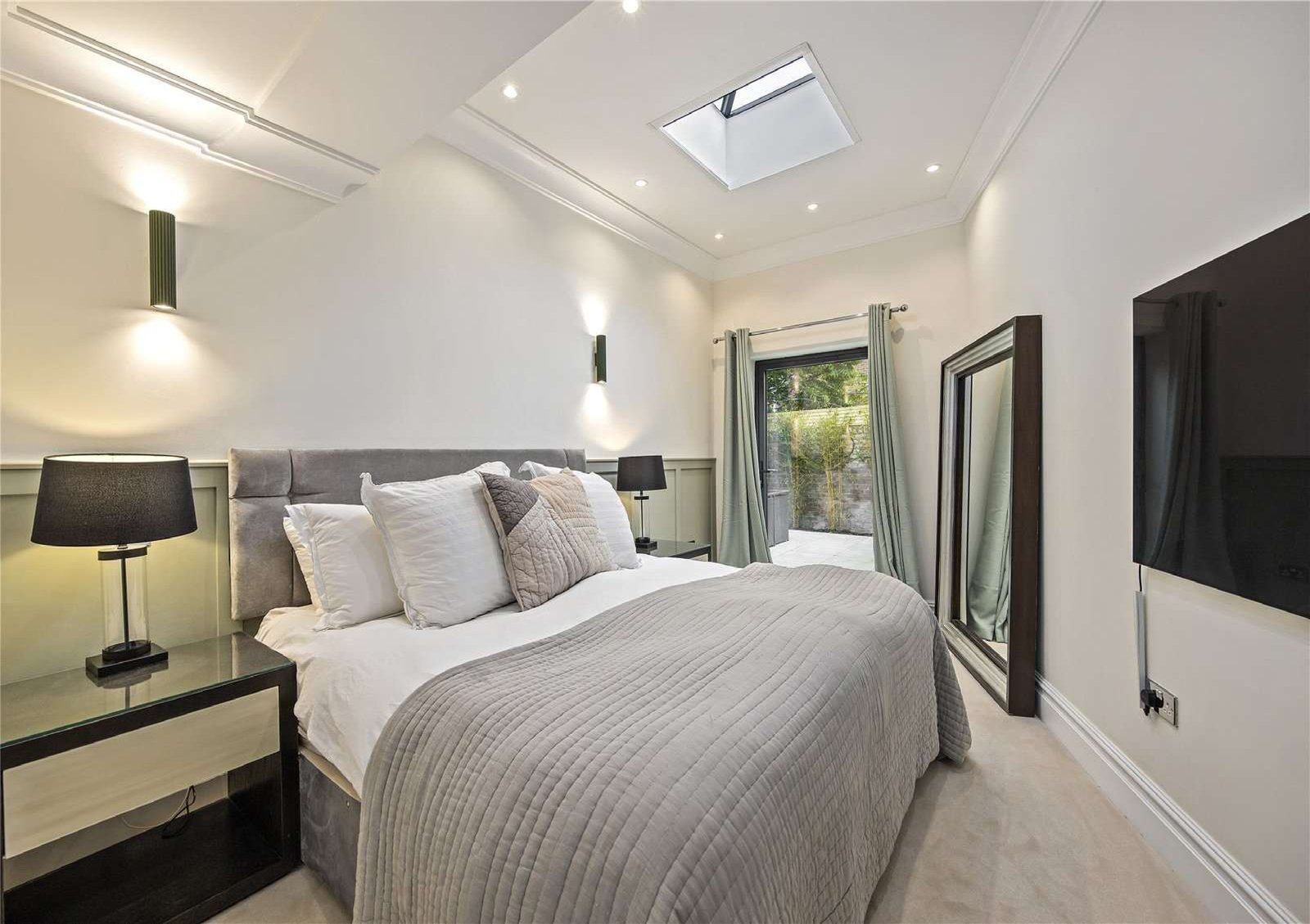 Master bedroom with neutral palette, panelled feature wall and wall-mounted TV — Flat 1.