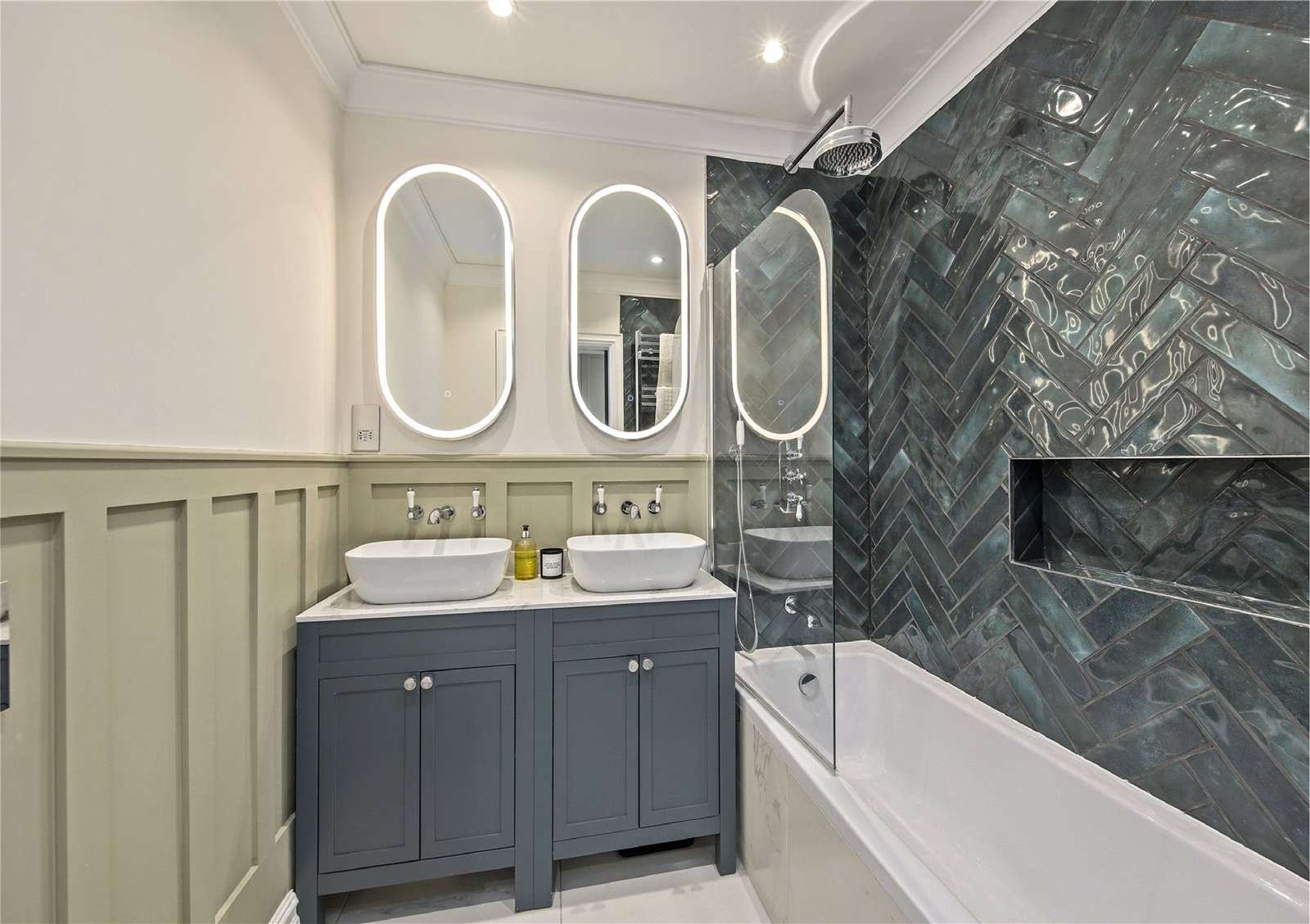 Bathroom with dark-green herringbone tile, double basin vanity and lit mirrors — Flat 1.