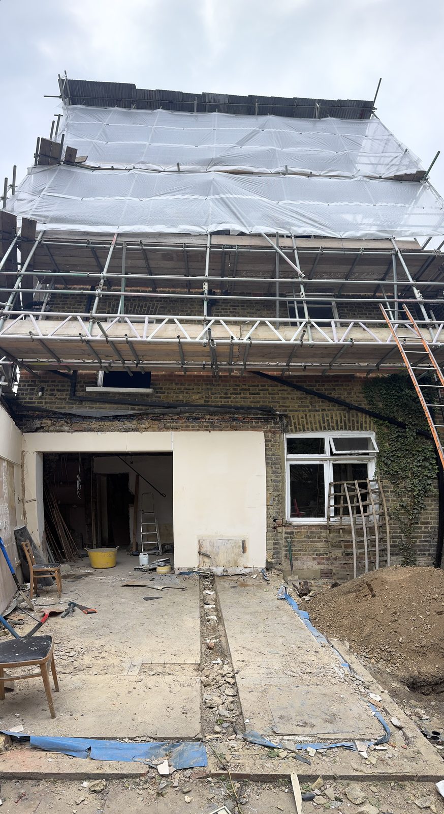 Rear of the building scaffolded mid-renovation, render stripped back and garden dug out — before, May 2025.