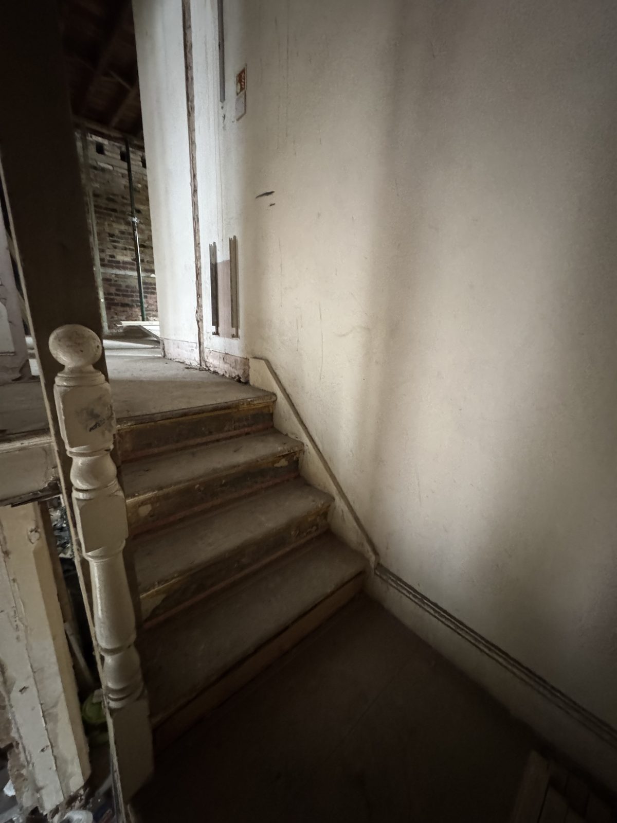 Original staircase stripped to bare treads and balustrade against bare plaster — before.