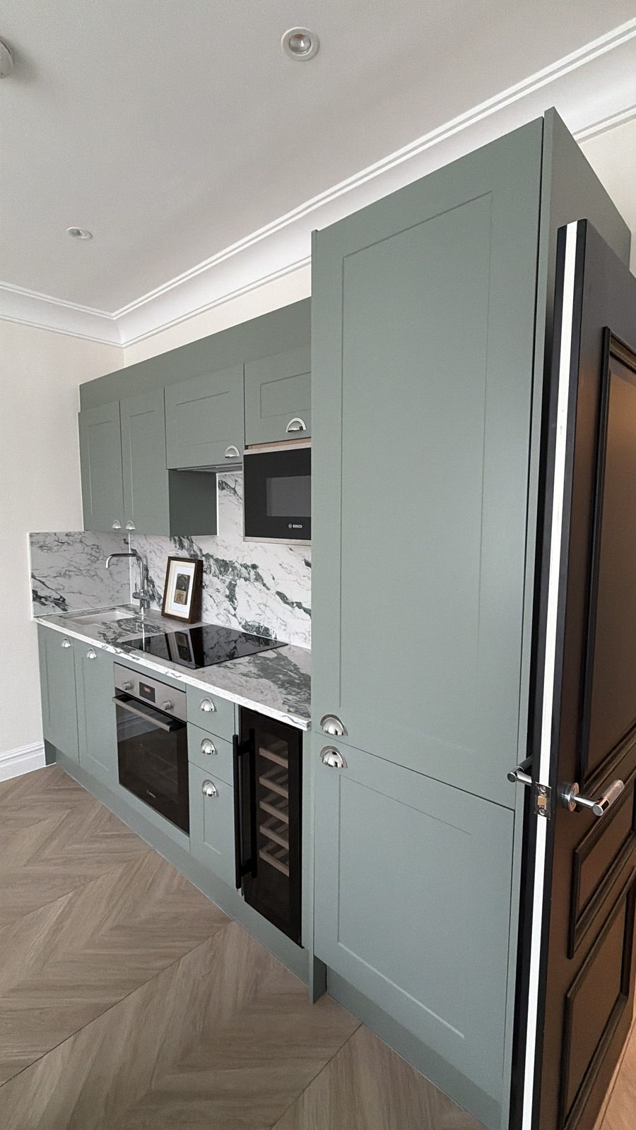 Kitchen with sage-green units, integrated appliances and herringbone parquet floor — Flat 2.